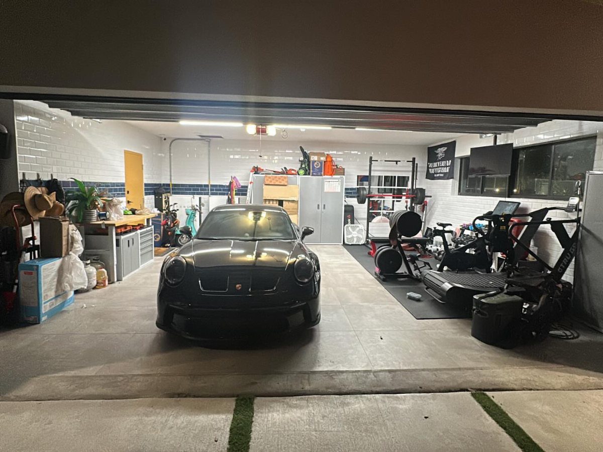 Black sports car parked in a garage containing gym equipment and a workshop area.