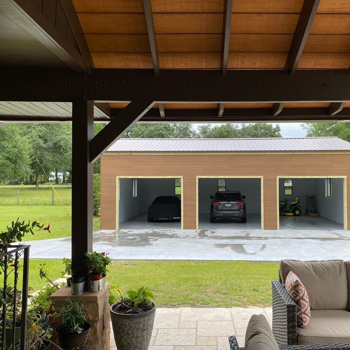 A tan three-bay pole barn garage containing a car, SUV, and lawn tractor on a concrete slab.
