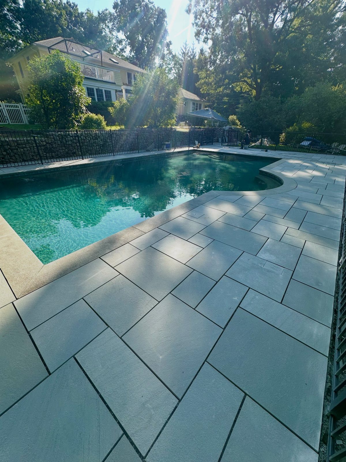 11 Flagstone Patio Design Ideas with Photos for Your Yard 9 Blue rectangular flagstone pavers surround a clear swimming pool in a sunny backyard setting.