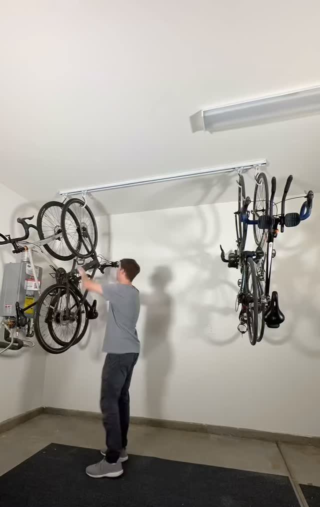 A man hanging a bicycle onto a white ceiling-mounted storage rack in a garage.