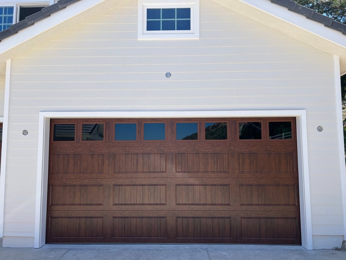 A dark wood-grain garage door with small window panes on a beige building.