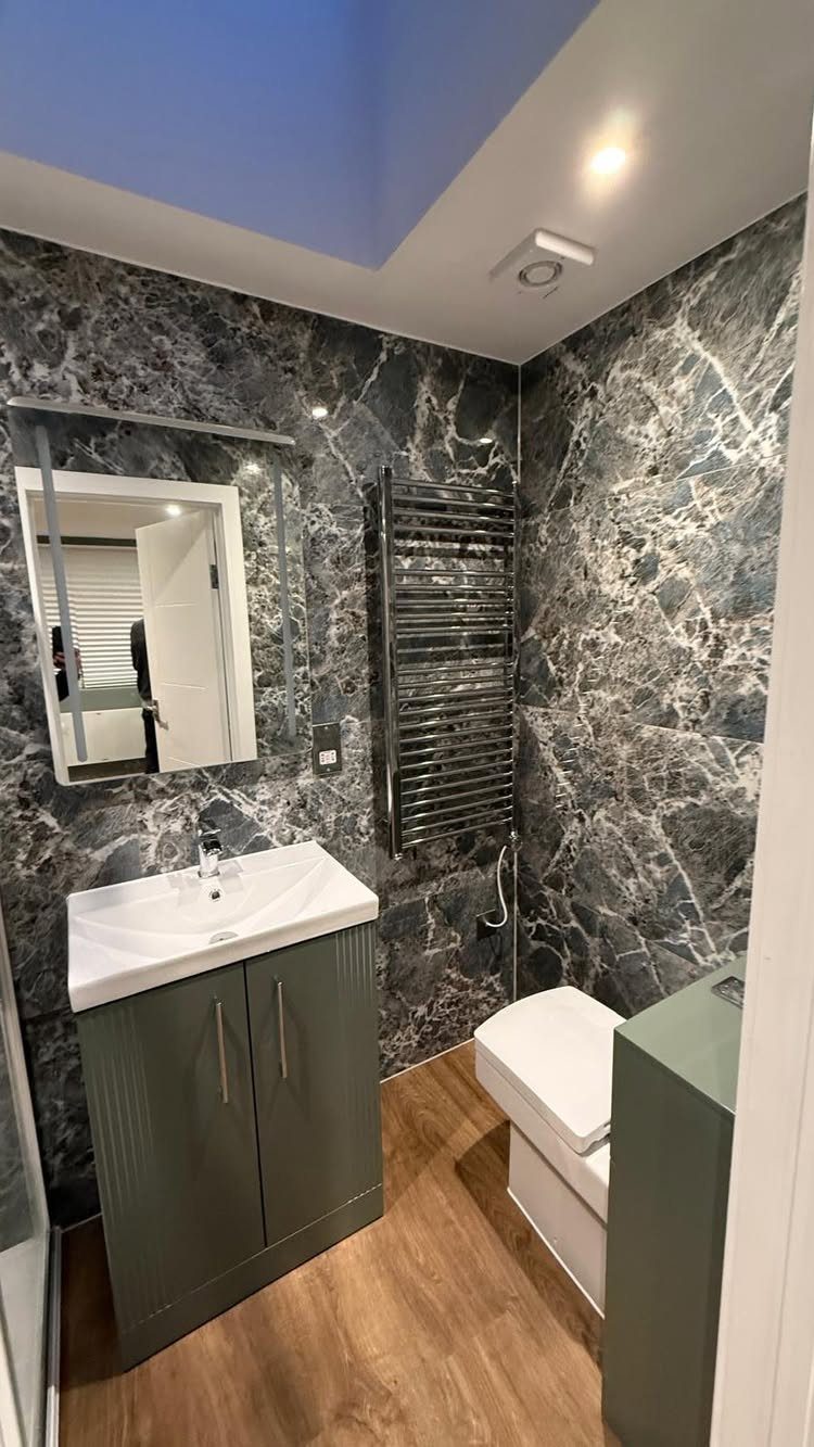 A modern small bathroom with dark marble walls, a grey vanity, and a white toilet.