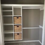 White melamine closet shelving unit with three woven storage baskets in a built-in organizer.
