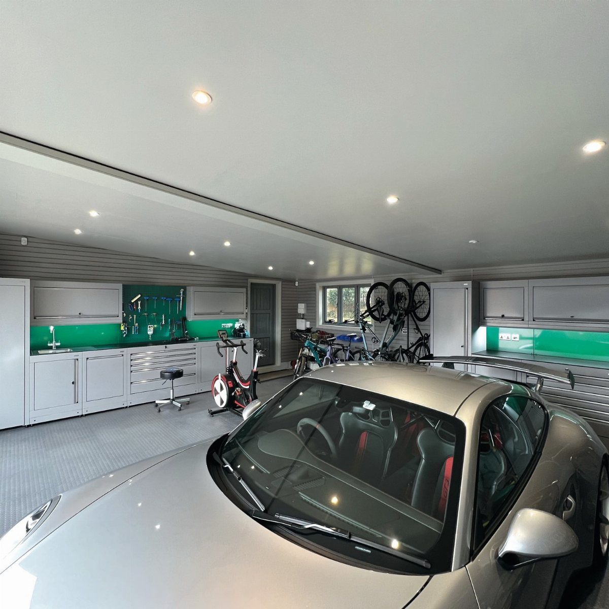 Silver sports car parked in a modern garage with gym equipment and workshop cabinetry.