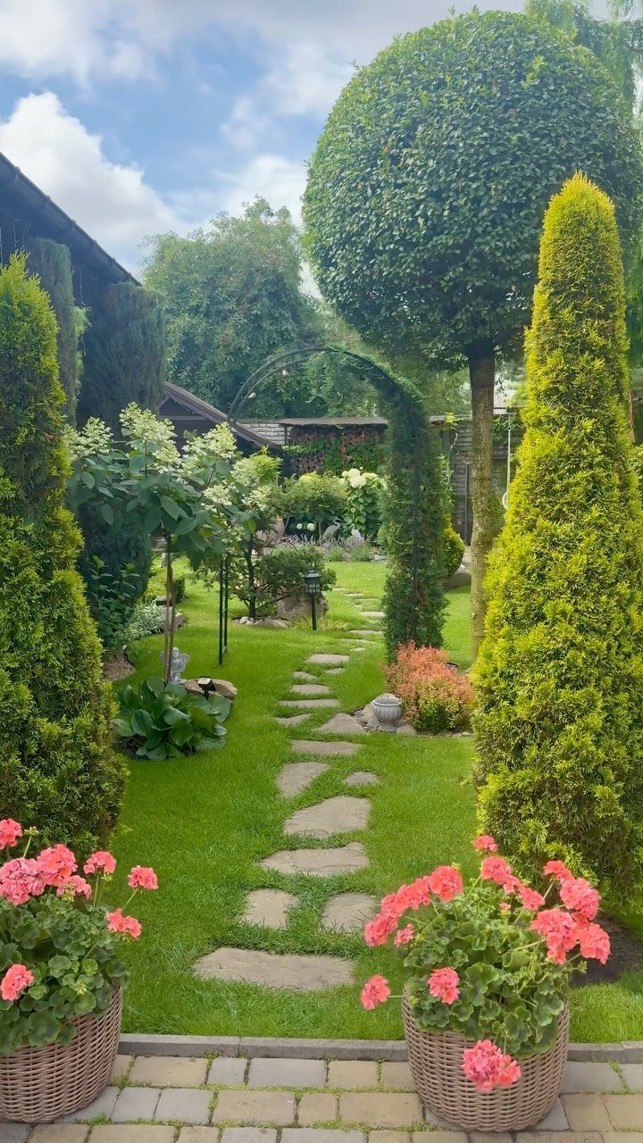 Manicured evergreen shrubs and a stone path winding through a lush green garden landscape.