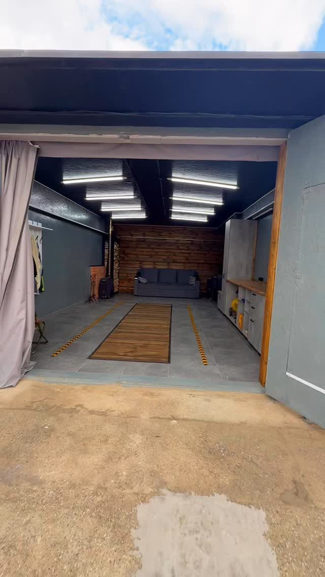 Converted garage space with grey tiles, a wooden floor runner, and bright overhead lighting.