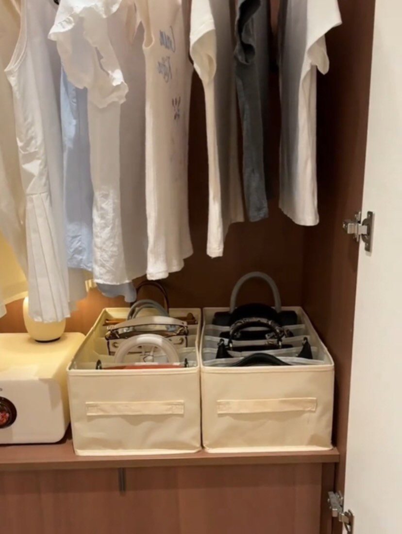 Handbag Storage and Display: 8 Ideas for Every Space 6 Cream fabric storage bins containing several handbags sitting on a wooden closet shelf below hanging shirts.