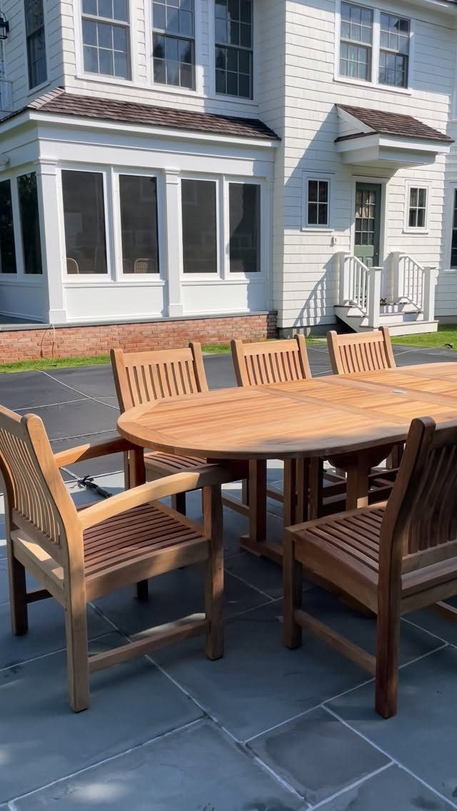 11 Flagstone Patio Design Ideas with Photos for Your Yard 4 Wooden dining table and chairs set on a grey flagstone patio outside a white house.