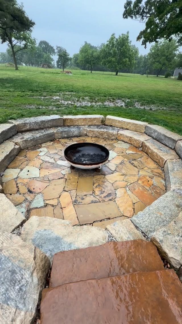 11 Flagstone Patio Design Ideas with Photos for Your Yard 1 A circular flagstone patio with a black fire bowl centered within a stone retaining wall.