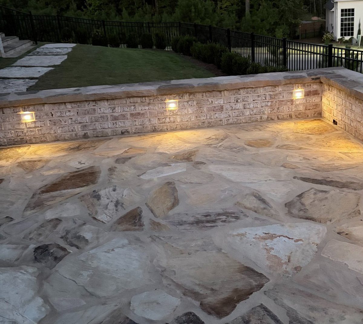 11 Flagstone Patio Design Ideas with Photos for Your Yard 11 Flagstone patio with built-in low-voltage lights on a stone retaining wall at night.