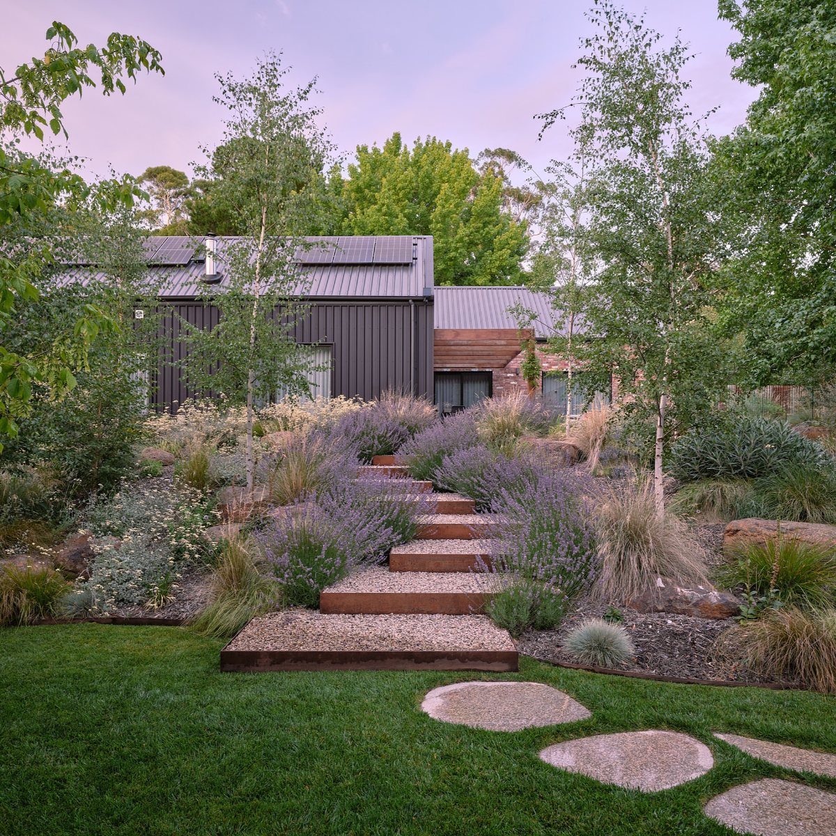 11 Flagstone Patio Design Ideas with Photos for Your Yard 10 Wooden garden steps and circular stepping stones lead through lavender plants toward a modern house.