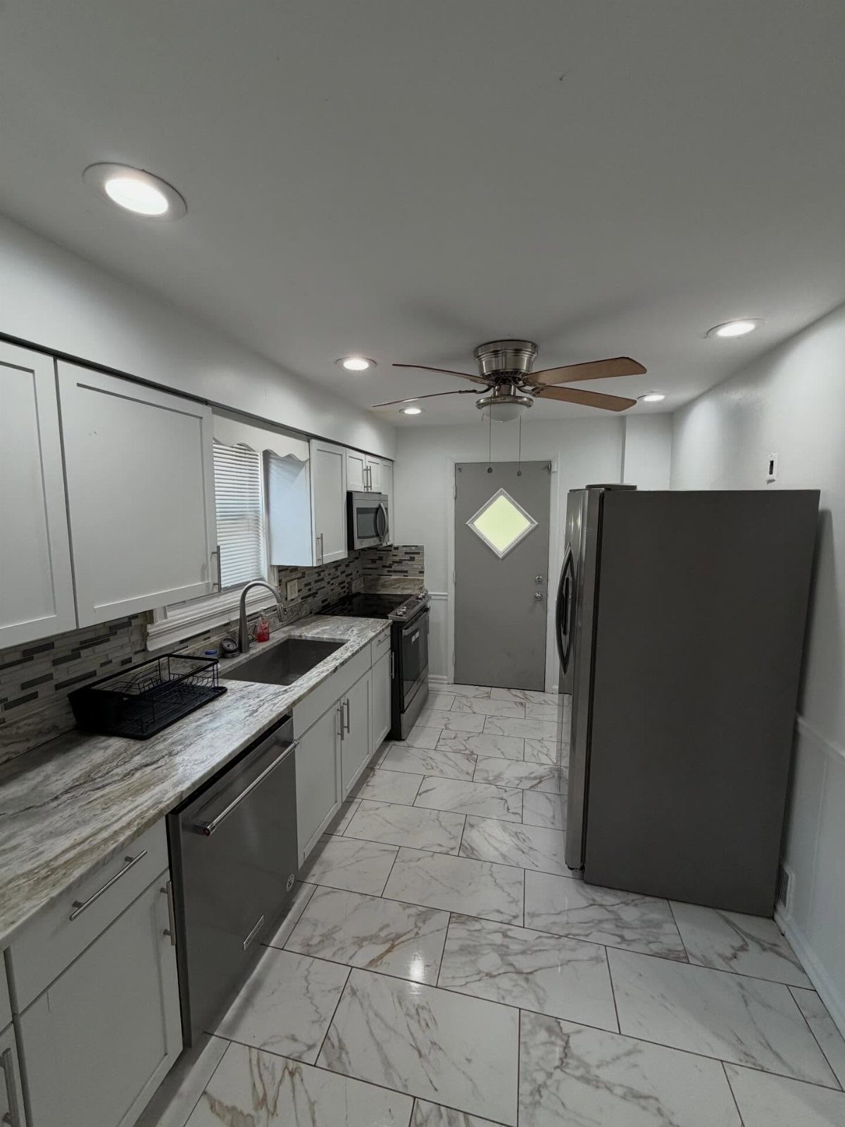A modern kitchen featuring white cabinets, marble countertops, and stainless steel appliances with marble flooring.