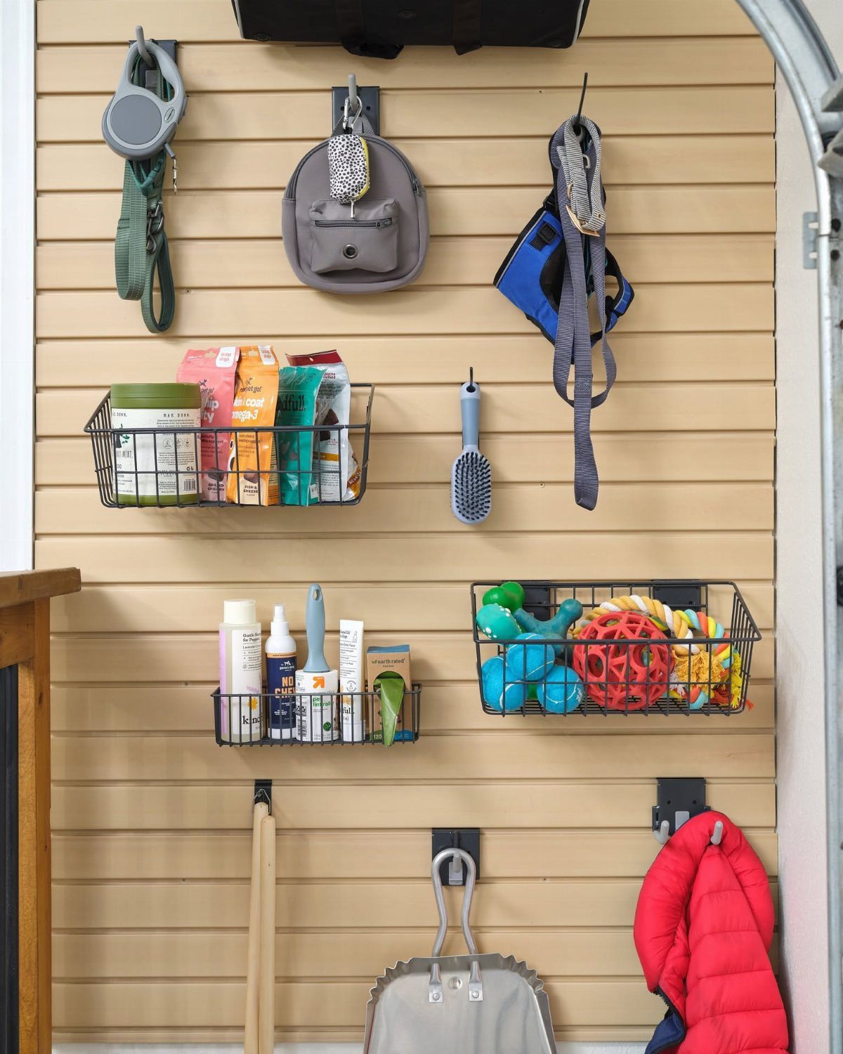 Pet supplies hanging on a tan slatwall organizer including leashes, food, and toys.