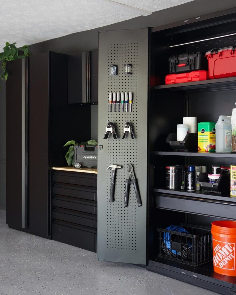Modern black garage storage cabinets, pegboard with tools, and organized shelving units against a dark wall.