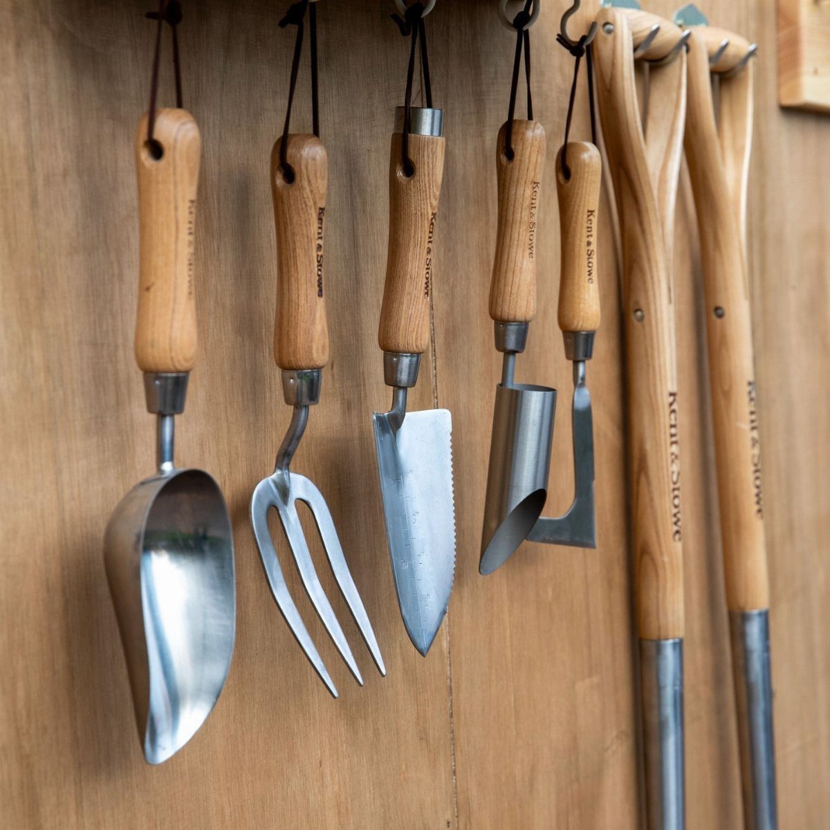 11 Garden Tool Organization Ideas for a Neater Shed or Garage 9 Small wooden-handled garden hand tools hanging vertically against a light brown wooden wall.