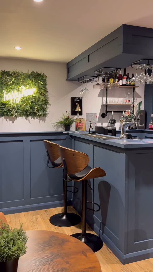 A modern blue home bar with wooden stools and a green plant wall decoration.
