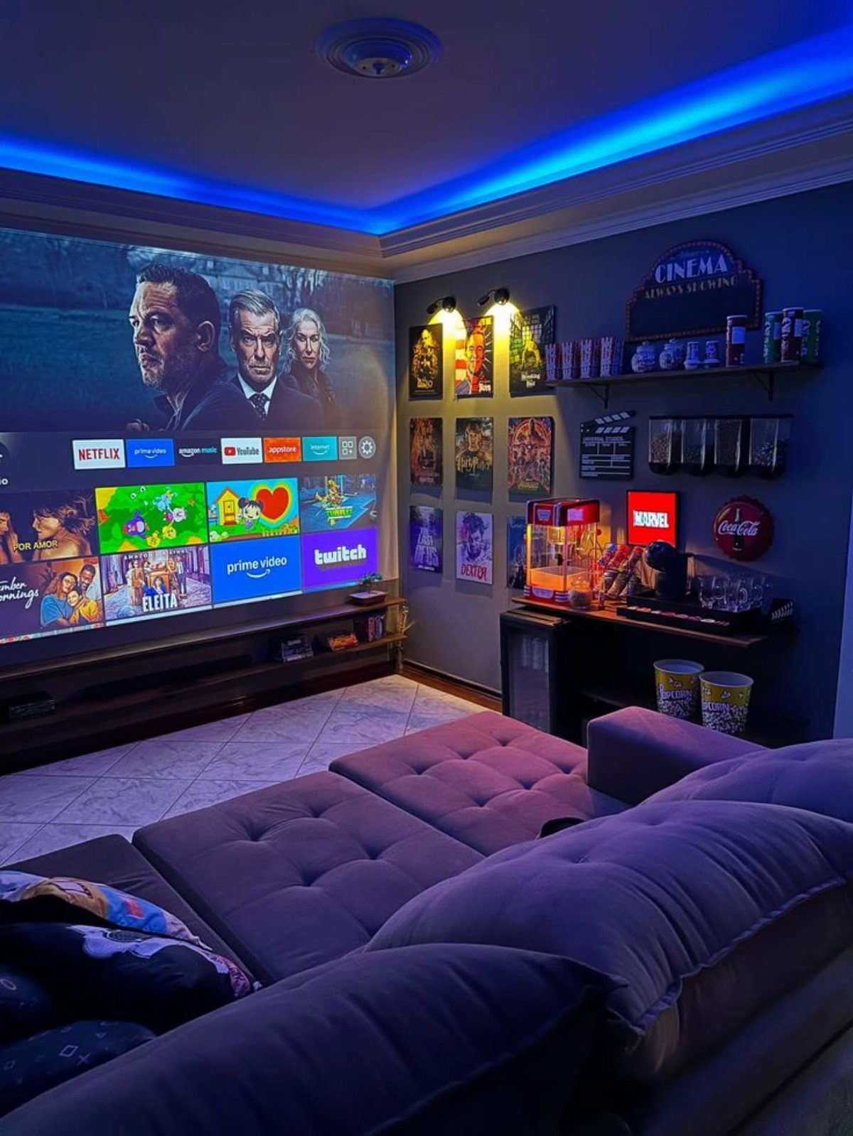 A cozy home theater room with a large screen, blue LED lighting, and a purple sectional sofa.