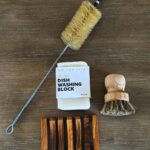 Natural bristle dish brushes, a soap block, and a wooden soap dish on wood.