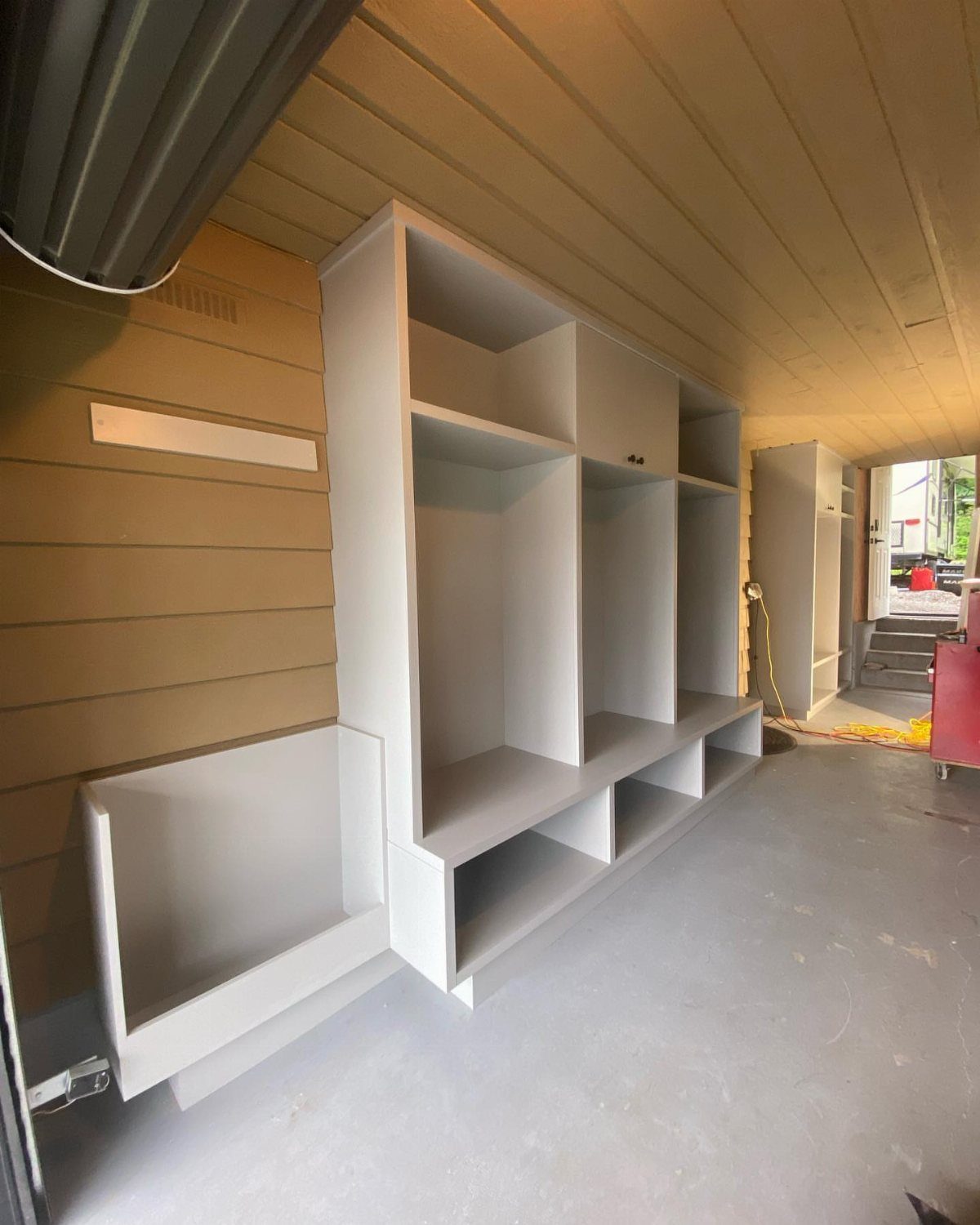 Garage Storage Modern: 12 Ideas That Free Up Floor Space 12 White built-in storage shelves and cabinets installed against a tan wood-paneled garage wall.