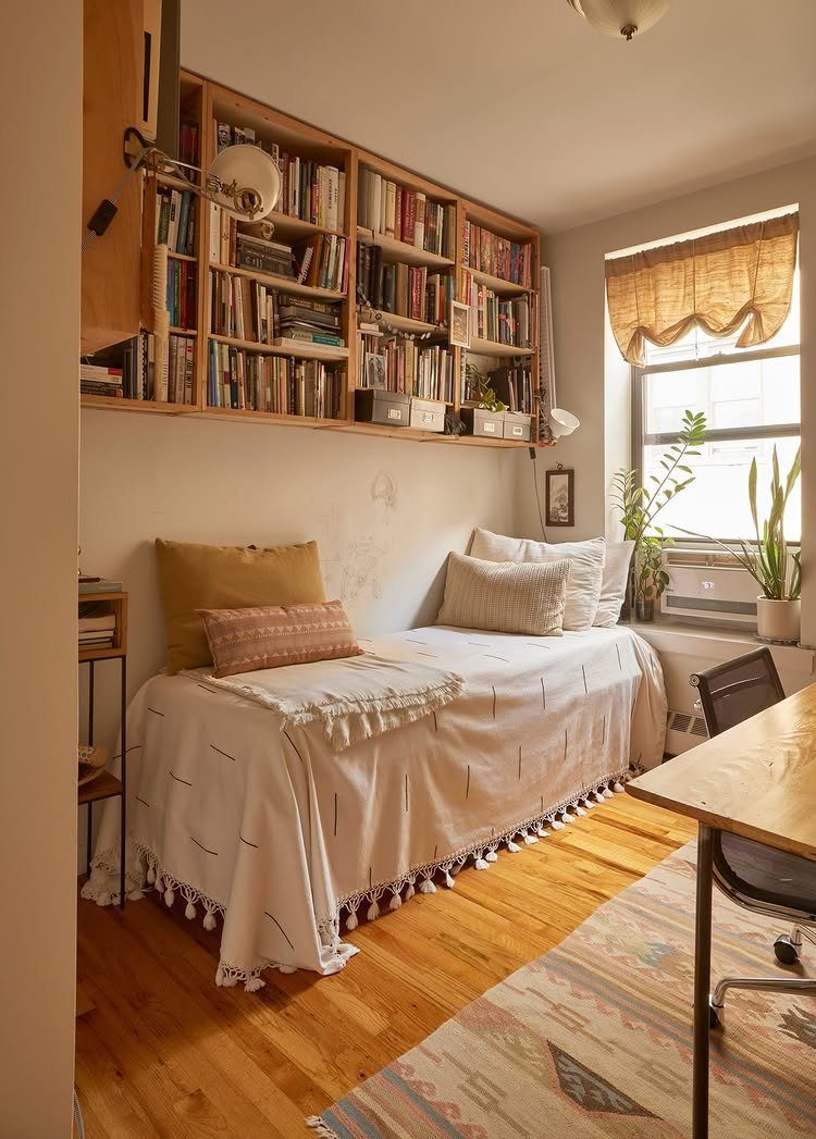 Studio Apartment Organization: 9 Ideas That Save Space 7 A small studio apartment bedroom with a bed tucked under high wall-mounted bookshelves and a desk.