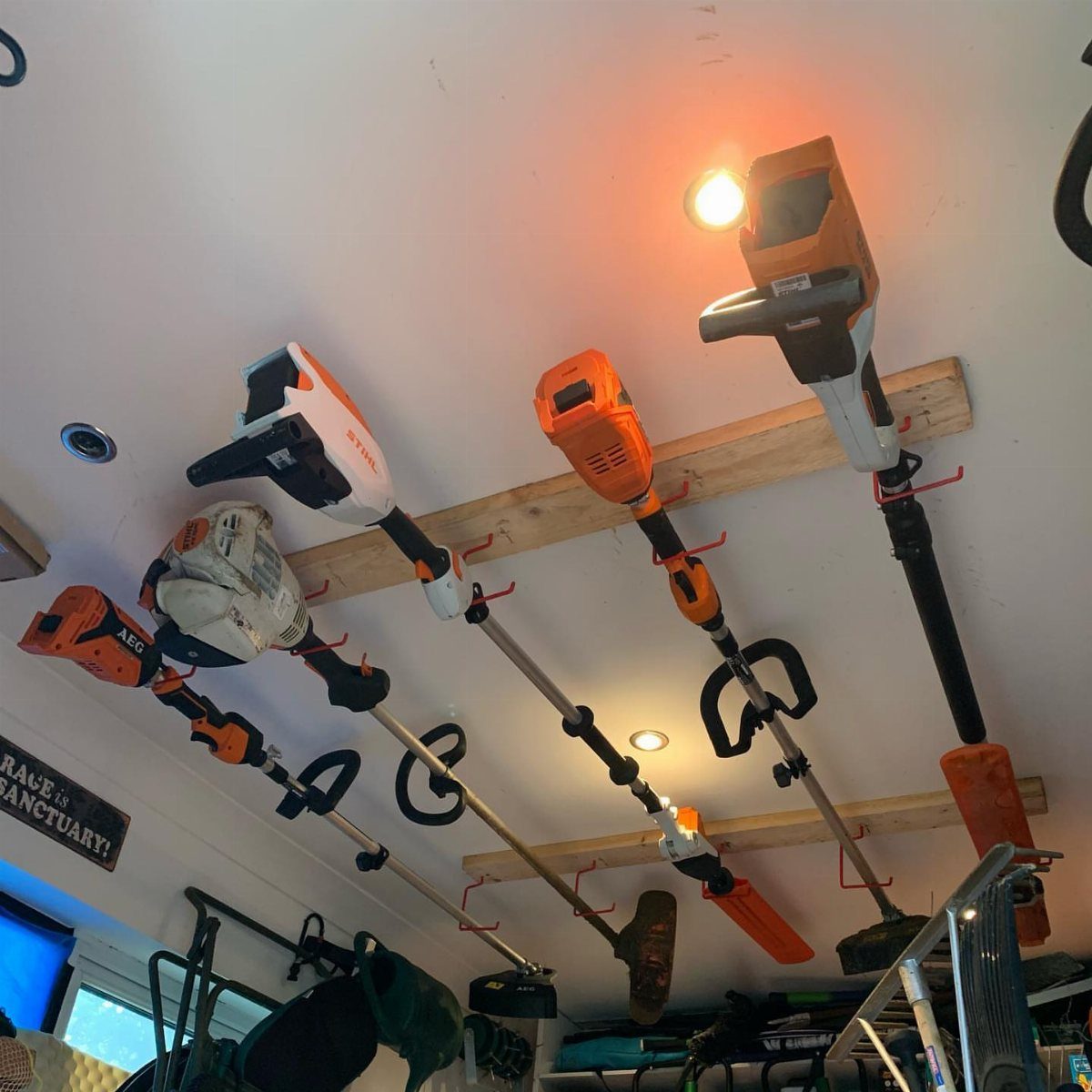 11 Garden Tool Organization Ideas for a Neater Shed or Garage 3 Garden tools hanging from wooden beams mounted to a white ceiling using red hooks.