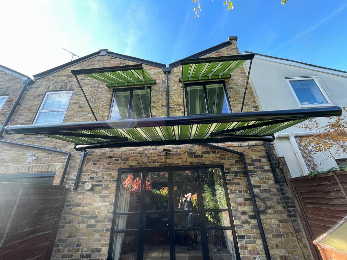 Two green and white striped retractable awnings attached to a brick house above glass doors.