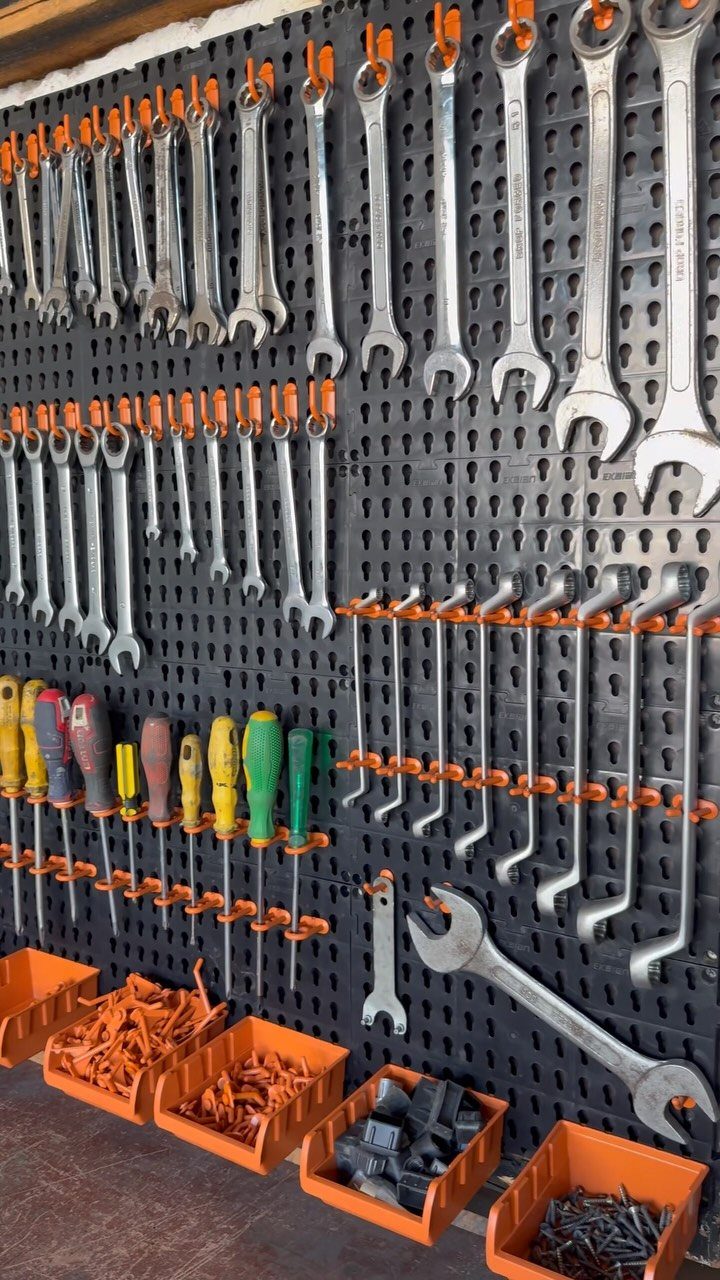 Metal wrenches and screwdrivers organized on an orange hook pegboard system above hardware bins.