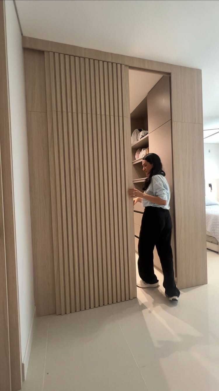 Master Closet Design Layout: 13 Plans for Reach-In and Walk-In Spaces 12 A woman opening a slatted light wood sliding door to reveal a built-in closet interior.