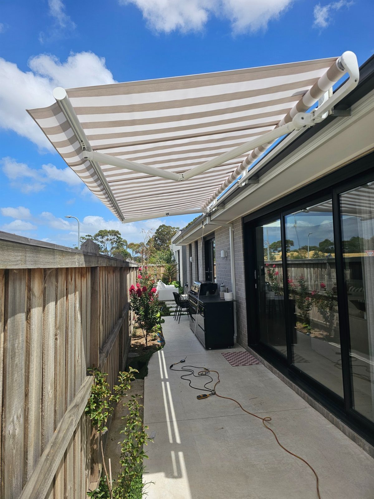 A striped retractable awning extended over a concrete patio next to a house with sliding doors.