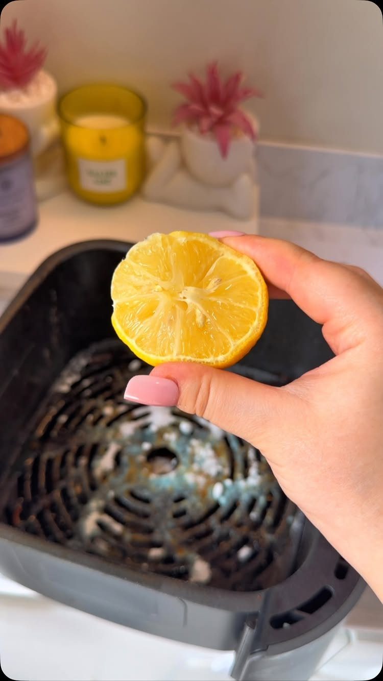 Home Cleaning Tips and Housekeeping: 13 Ideas That Save Time 6 A hand holding a lemon half over a dirty air fryer basket in a kitchen.