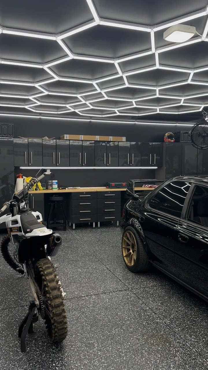 3 Car Pole Barn Garage with 6 Design Ideas 2 A black car and white dirt bike parked in a modern garage with hexagonal ceiling lights.