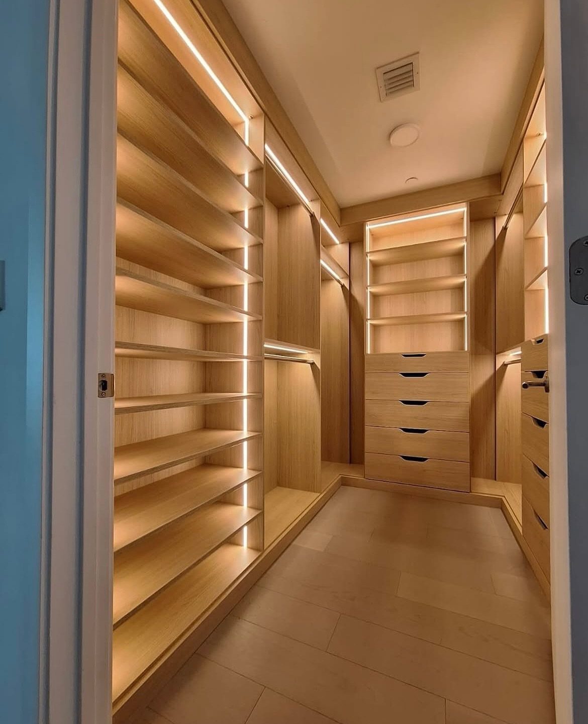 Master Closet Design Layout: 13 Plans for Reach-In and Walk-In Spaces 5 Light wood walk-in closet with integrated LED lighting strips on shelves and drawers.