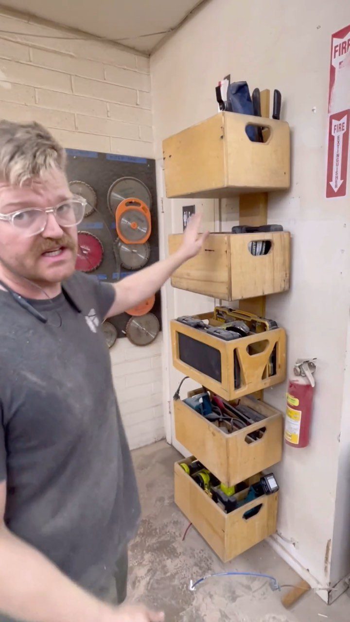 A man pointing at a vertical wall-mounted shelving system made of wooden crates.