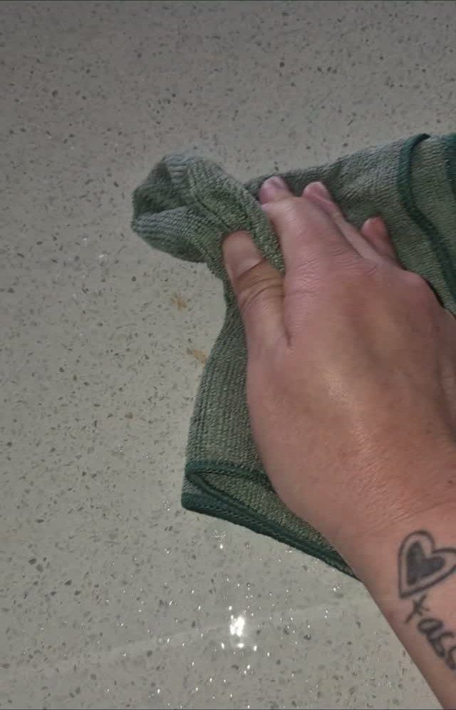 Home Cleaning Tips and Housekeeping: 13 Ideas That Save Time 5 A hand wiping a speckled countertop with a green microfiber cloth.