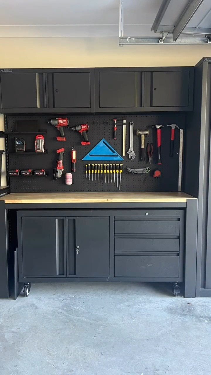 Black garage workbench with upper cabinets, pegboard holding tools, and lower storage cabinets on wheels.