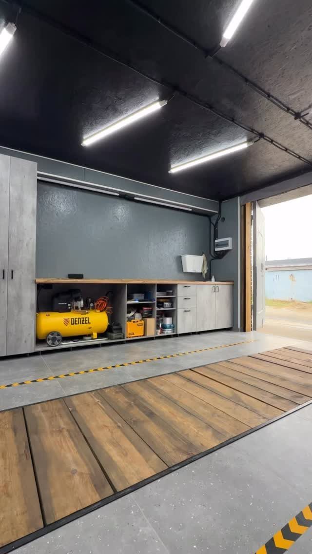 A modern garage workshop with a wooden workbench, grey cabinets, and a yellow air compressor.